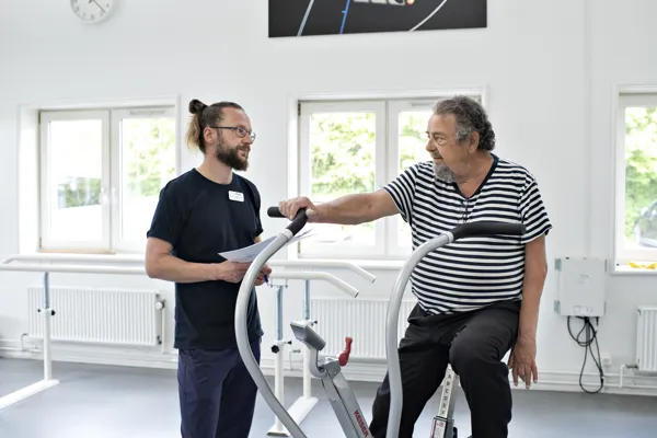 Fysioterapeut guider mand på motionscykel