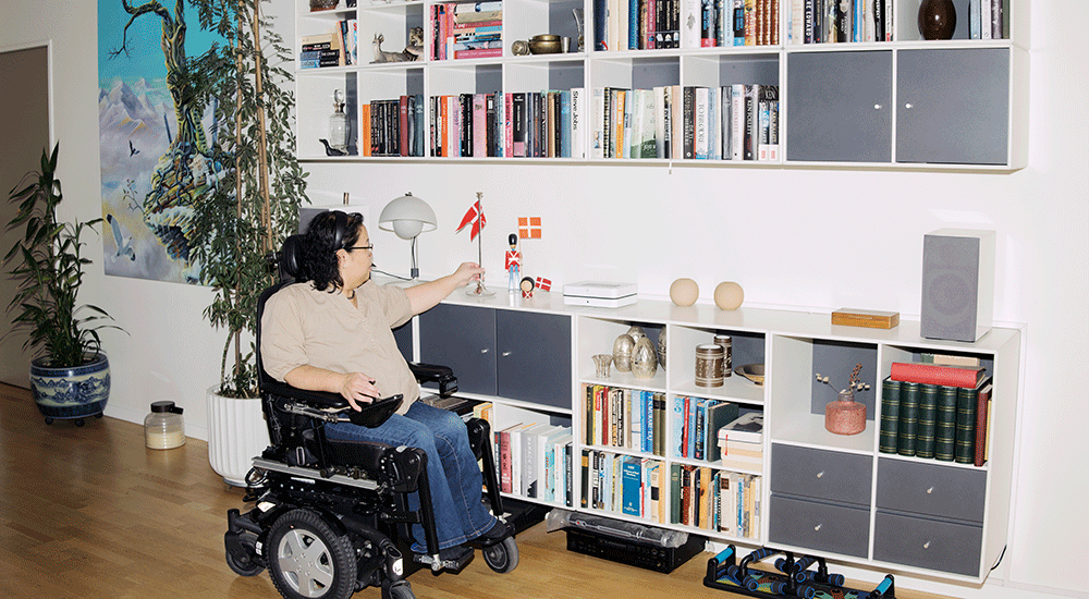 Tut Ma sidder i en kørestol foran sin bogreol.