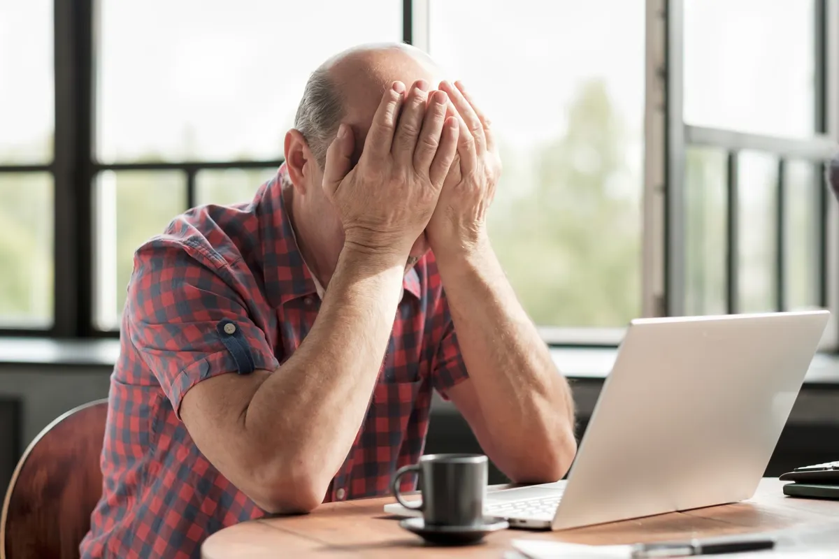 Udmattet aeldre mand, sidder ved bord foran sin computer