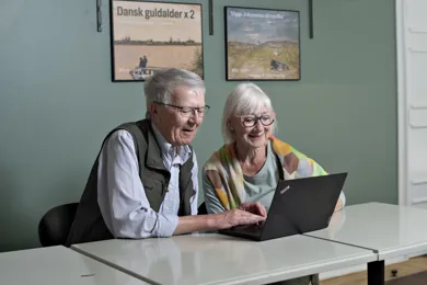 To ældre personer sidder og kigger på en computer.