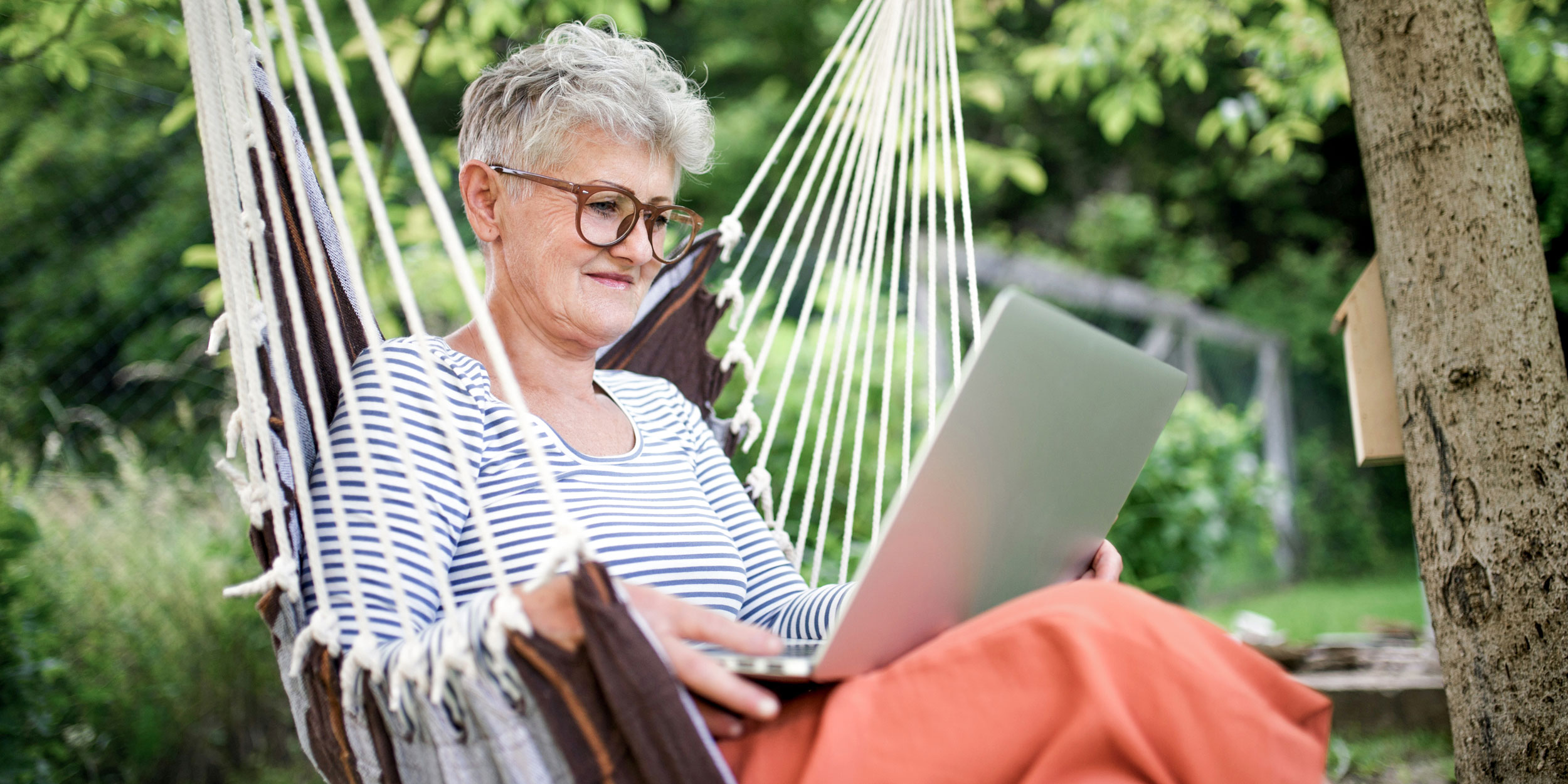 Kvinde sidder med computer udenfor i en haengekoeje. 