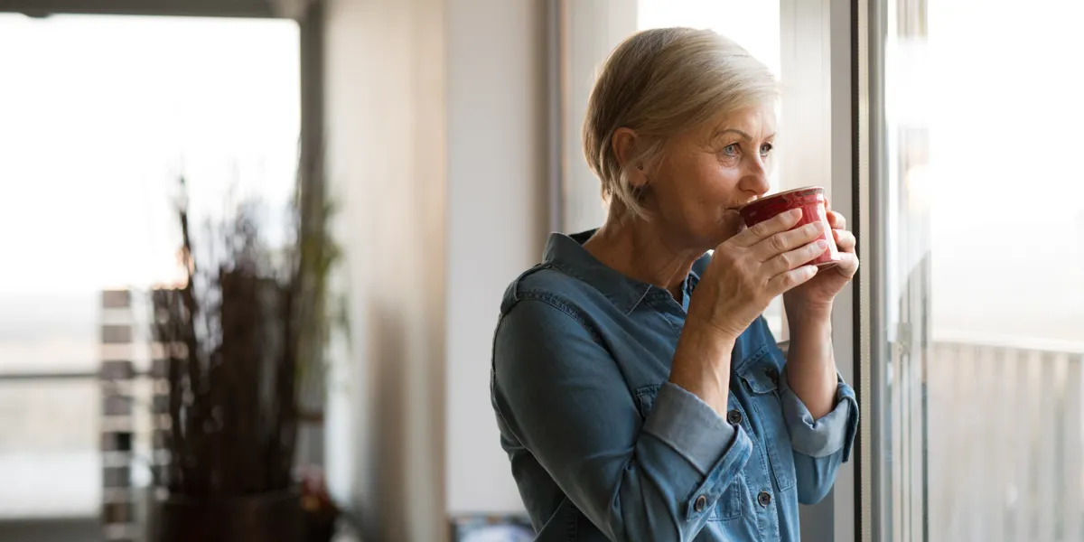 Kvinde drikker kaffe og kigger ud af vinduet.