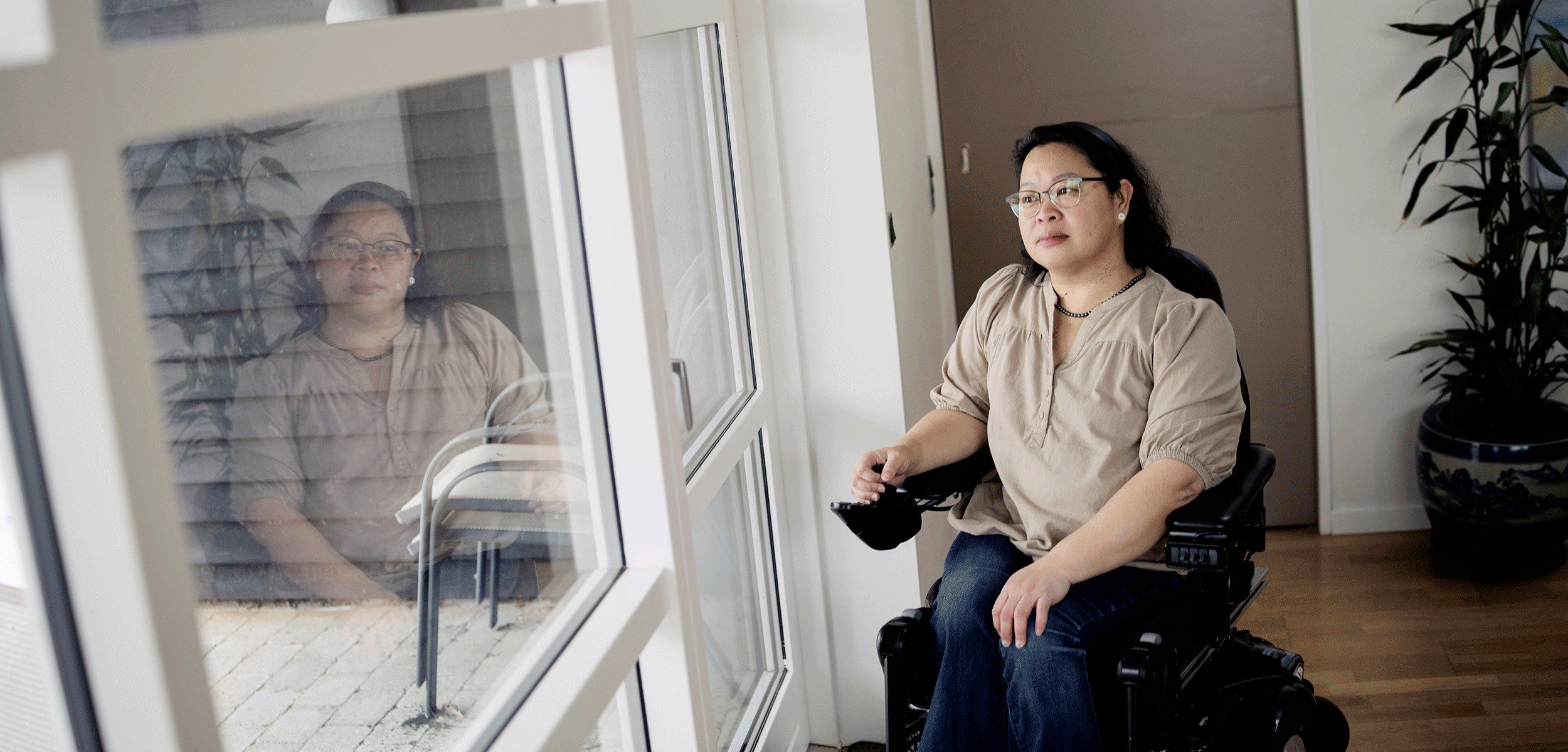 Tut Ma sidder i sin kørestol og kigger ud af et stort vindue