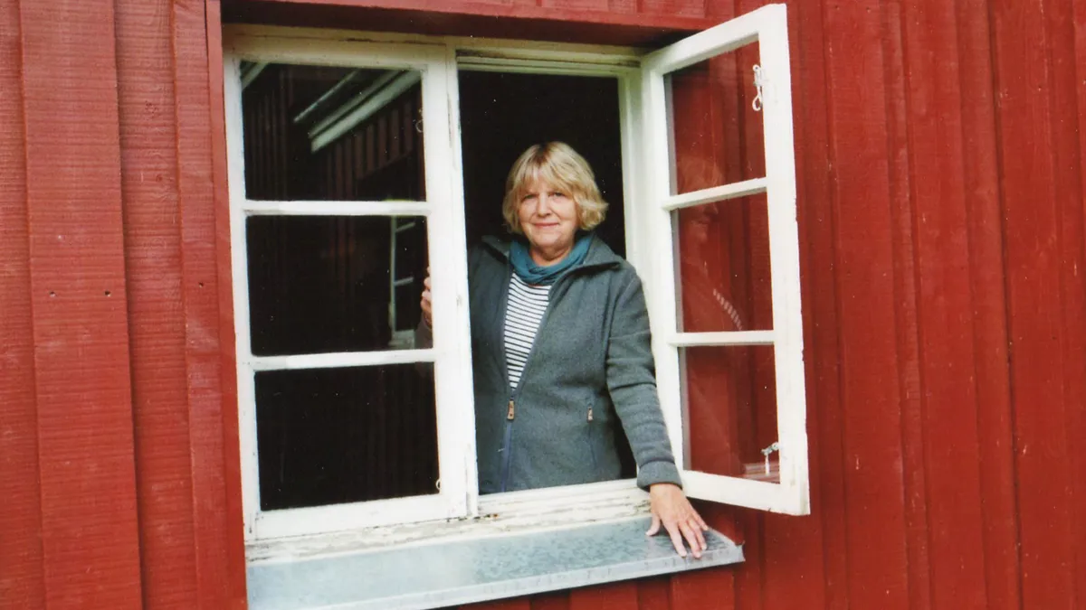 Jorunn står i åbent vindue i rødt hus